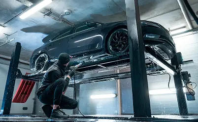 Mężczyzna myjący maszyną ciśnieniową samochód na podnośniku